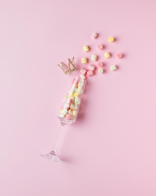 Crumbling pieces of marshmallow from a glass glass and a golden crown on a pink background. The concept of Valentine's Day. Flat lay.