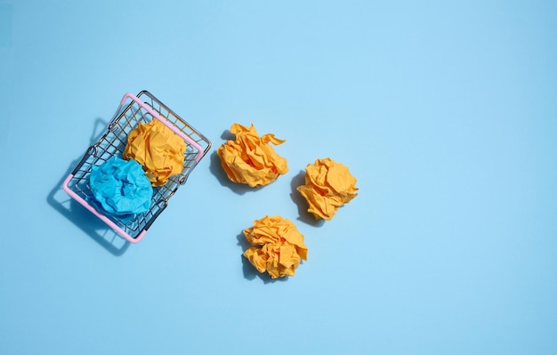 Crumpled balls of paper in a miniature shopping cart on a blue background New ideas and innovations