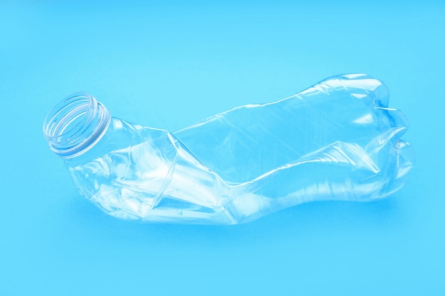 Crumpled plastic bottle on blue background. Environmental plastic pollution