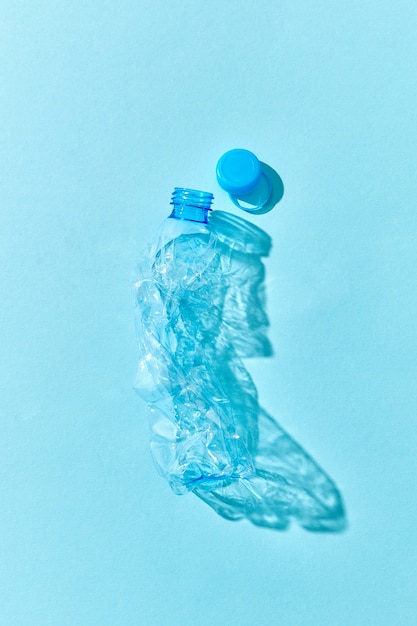 Crumpled plastic bottle with shadows on a pastel blue wall. Concept enviroment pollution of plastic.