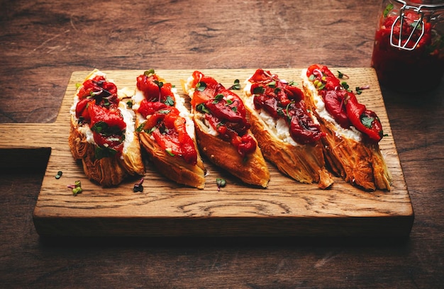 Crunchy bruschetta with soft cream cheese and sweet red paprika in olive oil with herbs served on cutting board on rustic wood kitchen table background top view