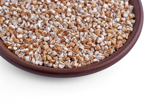 Crushed wheat or barley groats in a brown ceramic bowl isolated on a blue background