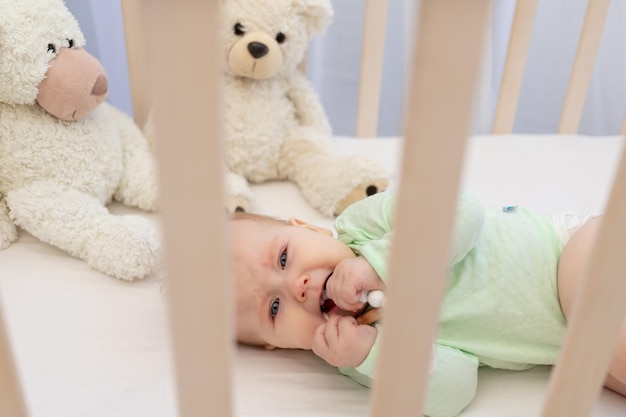 A crying baby in a crib with a teether in the bedroom