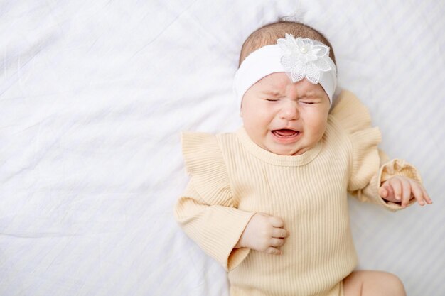 Crying newborn baby girl in a crib at home on a white cotton bed at home