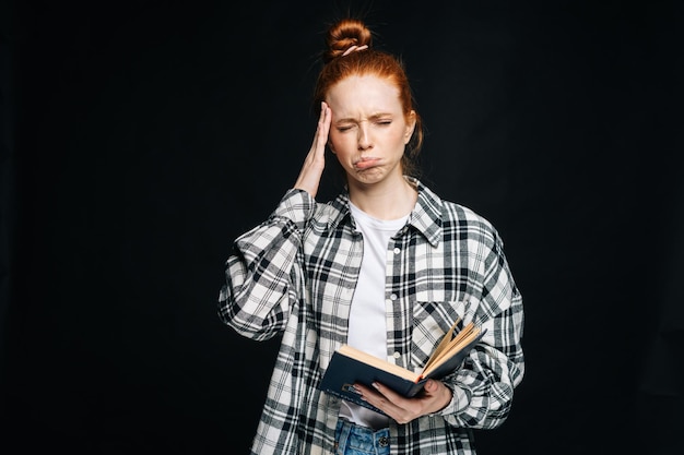 Crying upset young woman college student with headache holding book and touching temples