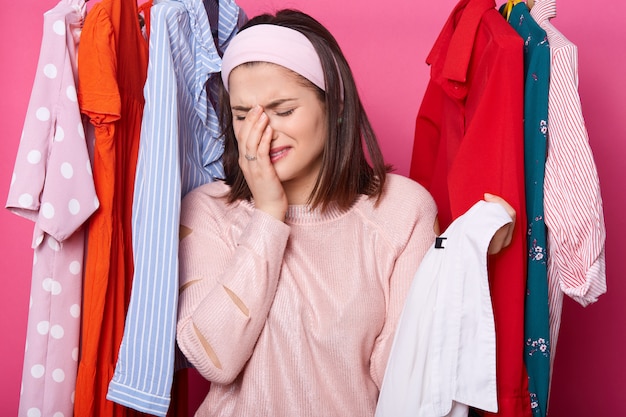 Crying woman keeping right hand near her face and holding hanger with white shirt while