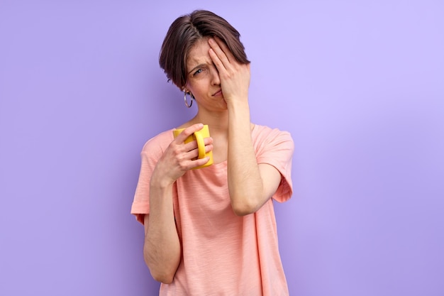 Crying woman need more rest female is tired by work doesnt want to go work or studying holding mug or cup in hands isolated purple background