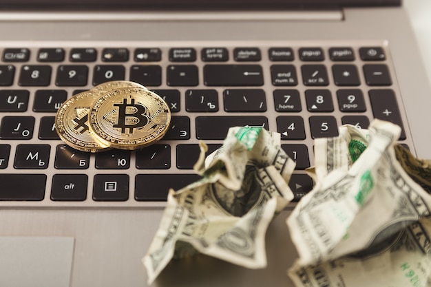 Crypto currency. Gold bitcoin coins and crumpled dollars on laptop keyboard