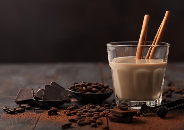 Crystal glass of Irish cream baileys liqueur with cinnamon coffee beans and powder with dark chocolate on dark wood background Space for text