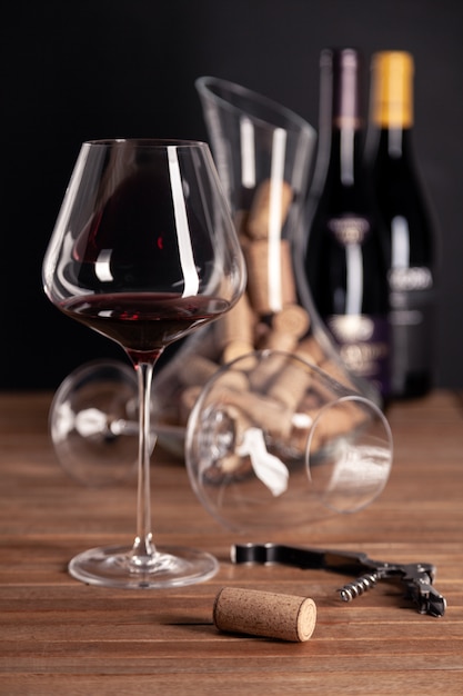 Crystal glass of red wine, bottles, corkscrew, decanter, corks on wooden table