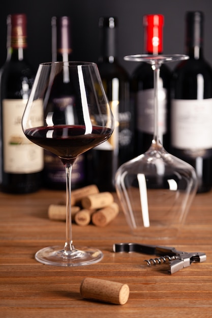 Crystal glasses of red wine, bottles, corkscrew, corks on wooden table