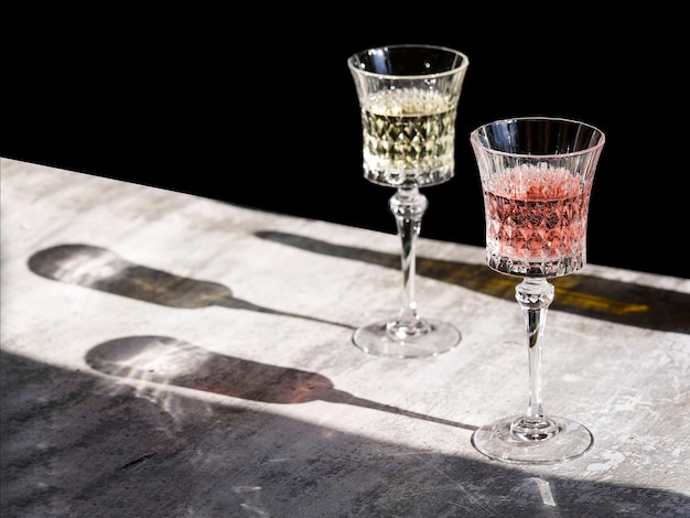 crystal wine glasses with white and rose champagne on gray background with hard lights and shadows