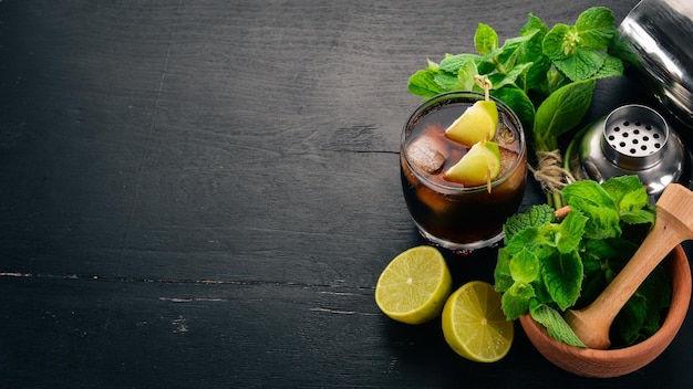 Cuba libre cocktail glass Lime mint On a black wooden background Free space for text