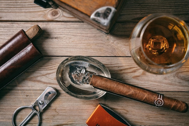 Cuban cigar and a glass of cognac brandy on wooden background top view