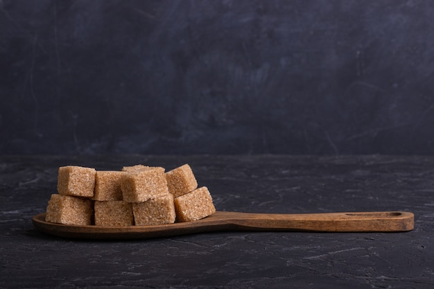 Cubes of cane sugar in a wooden spoon on a dark background