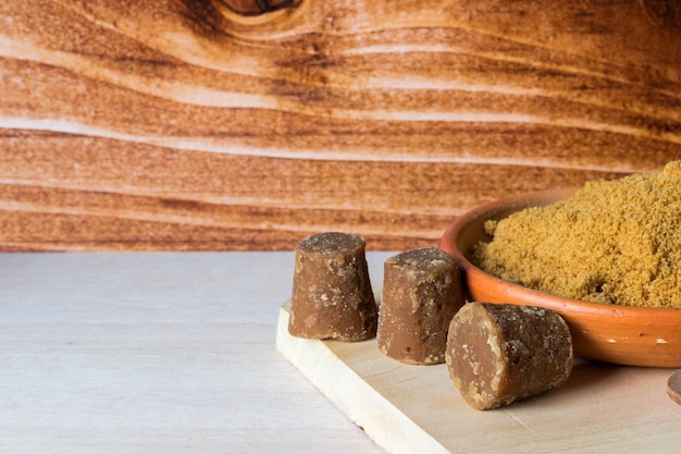 Cubes and powdered Panela or sweet sugar cane on a chopping board with wooden background typical food of Colombia