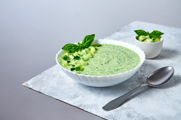 Cucumber gazpacho  cold summer soup with basil in white bowl on light background