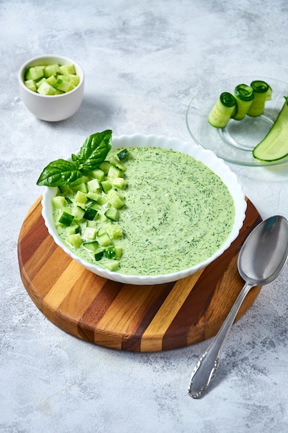 Cucumber gazpacho  cold summer soup with basil in white bowl on wooden board on light background