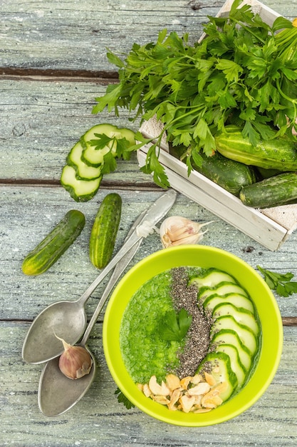 Cucumber Gazpacho. Green fresh cold summer soup. Fresh vegetables, greens, spices and cutlery. Old wooden boards background, top view