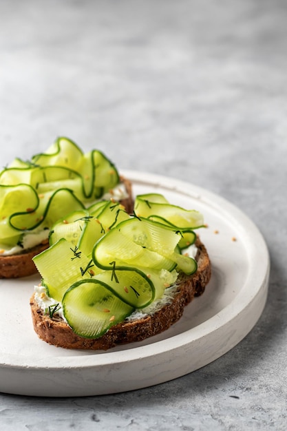 Cucumber sandwiches with soft cheese close up for delicious healthy vegetarian breakfast on gray background with text space