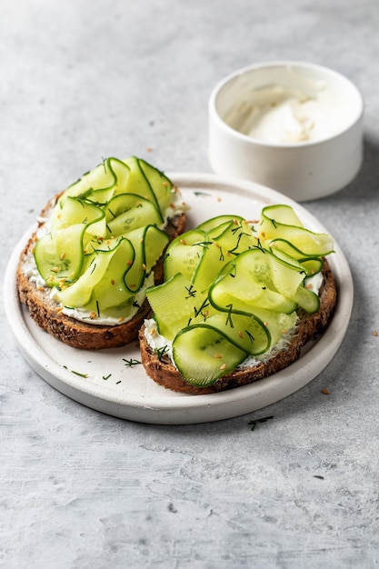 Cucumber sandwiches with soft cheese for delicious healthy vegetarian breakfast on gray background with text space