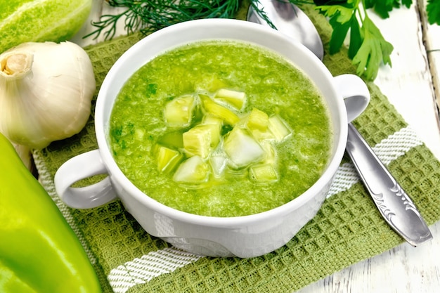 Cucumber soup with green peppers and garlic in a bowl on green napkin, parsley on the background light wooden boards