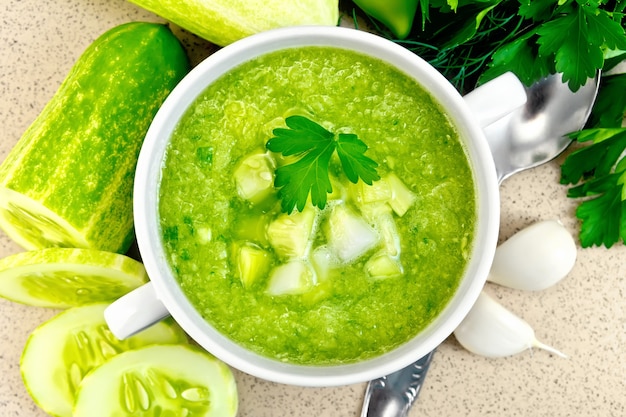 Cucumber soup with green peppers and garlic in a bowl, parsley on a background of a granite table top