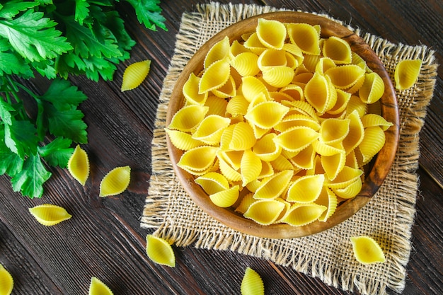 Culinary background with conchiglie pasta on wooden table. Pasta in the form of cockleshells