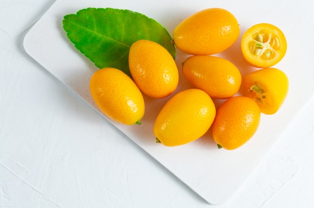 Cumquat or kumquat with green leaf on white wooden background.