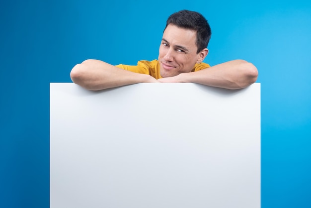 Cunning man leaning on blank banner in studio