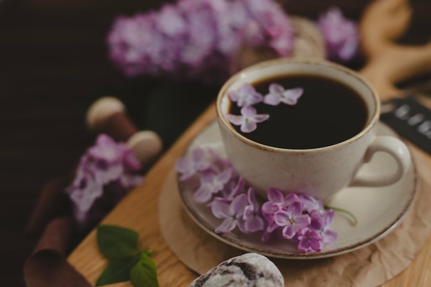 A cup of Americano black coffee purple lilac flowers on a wooden background A cup of Americano