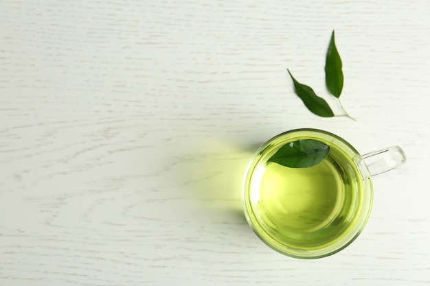 Cup of aromatic green tea and leaves on light wooden table flat lay Space for text