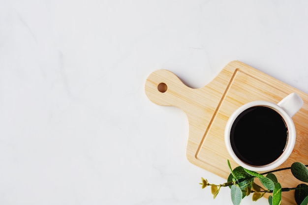 Cup of black coffee and artificial plant decor on wooden tray against 