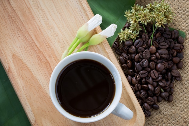 Cup of black coffee and coffee beans on wooden background.