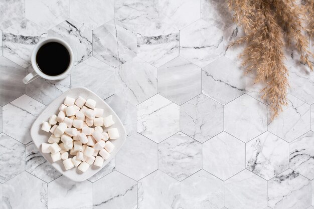 A cup of black coffee marshmallows on a plate and dry ears on a marble background