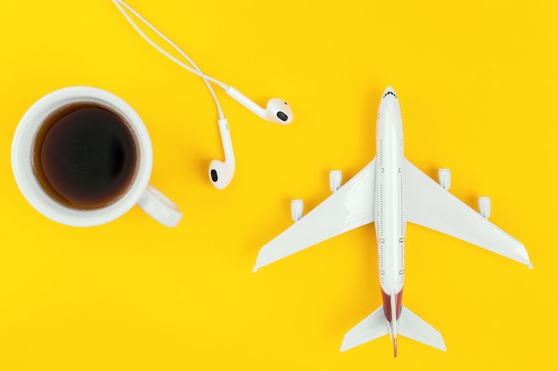 Cup of black coffee, plane and headphones on the yellow background.