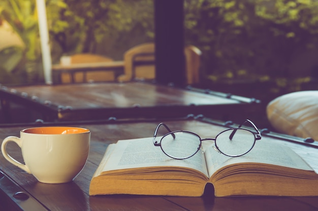 A cup of black coffee with reading glasses on table and open book in cafe