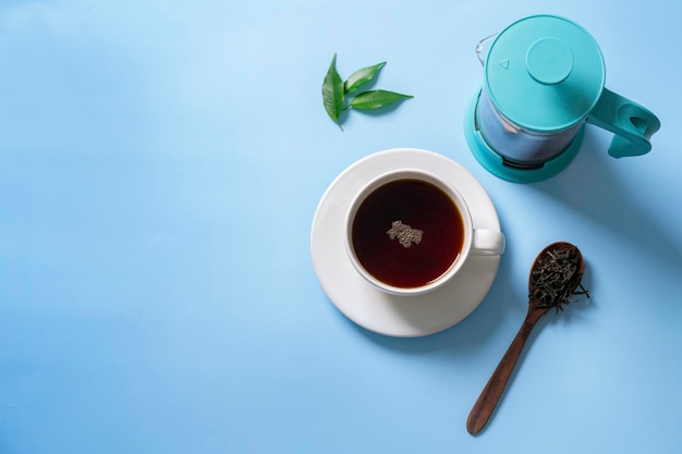 A cup of black hot tea with milk in jug and teapot stand on blue table with sunbeams View from above