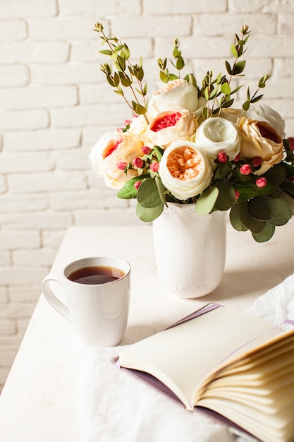 A cup of black tea, notebook and beautiful flowers on the table. Morning inspiration for the day planning