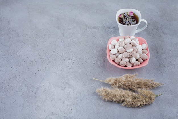 Cup of black tea with bowl of brown candies on stone background. 