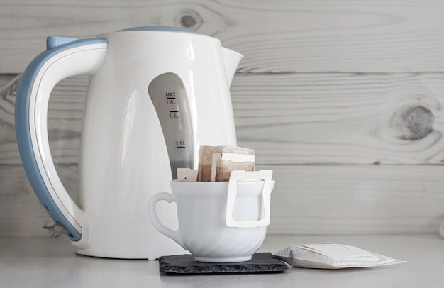 A cup of brewed natural coffee in a drip bag on the background of a teapot