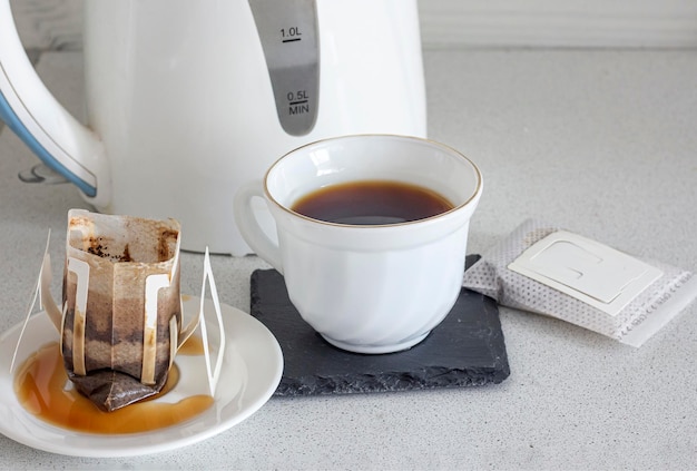 A cup of brewed natural coffee from a dropper bag on the background of a teapot closeup