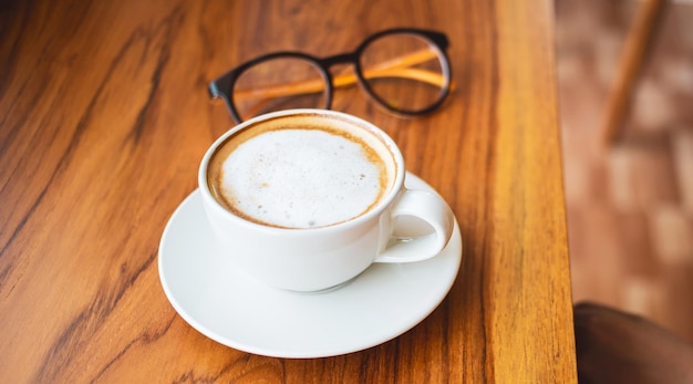 Cup of cappuccino coffee or  latte and glasses  on a wooden bar counter cafe in the morning