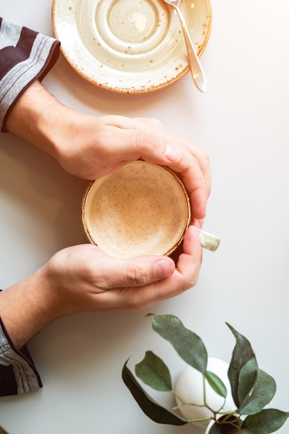 A Cup of cappuccino on a light table in a coffee shop in men's hands