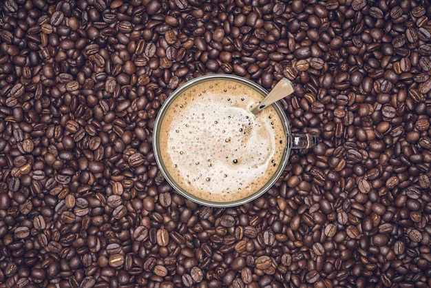 Cup of cappuccino placed in a plate of coffee beans, with Roasted Full frame coffee beans background