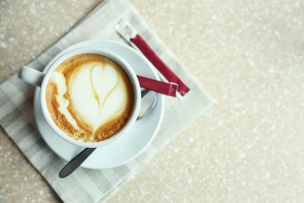 Cup of cappuccino with heart on foam on table in cafe