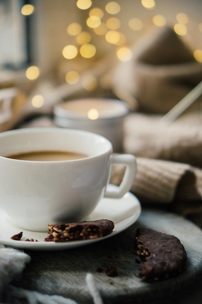 Cup of coffe with milk and chocolate cookies on warm wool blanket cozy winter home