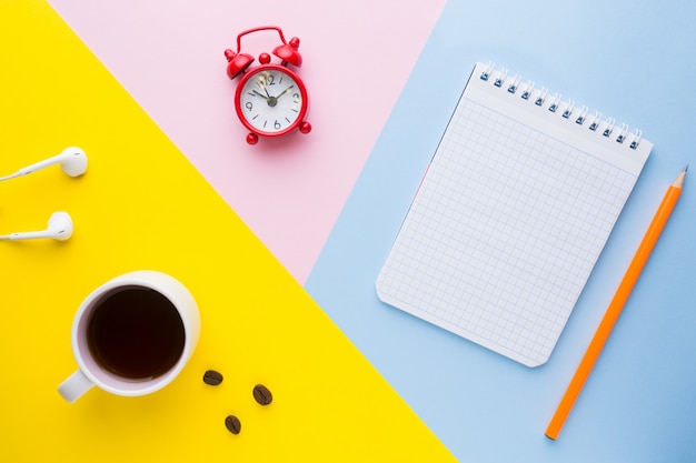 Cup of coffee, an alarm Clock And a notebook with a pencil