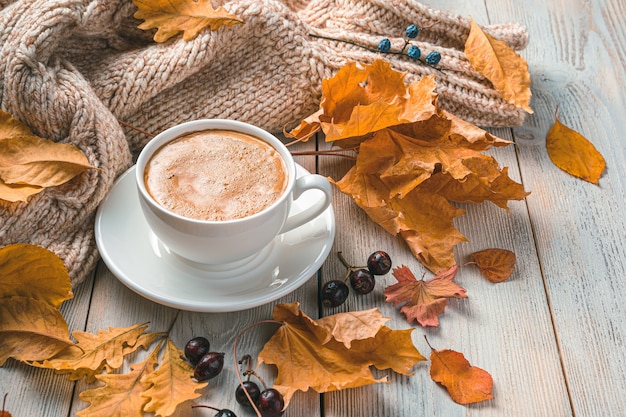 A cup of coffee on an autumn morning against the background of foliage and a sweater