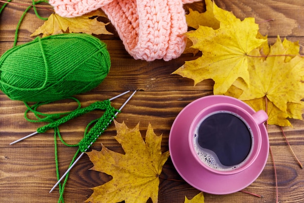 Cup of coffee ball of yarn knitting knitted scarf and yellow maple leaves on wooden table Autumn still life